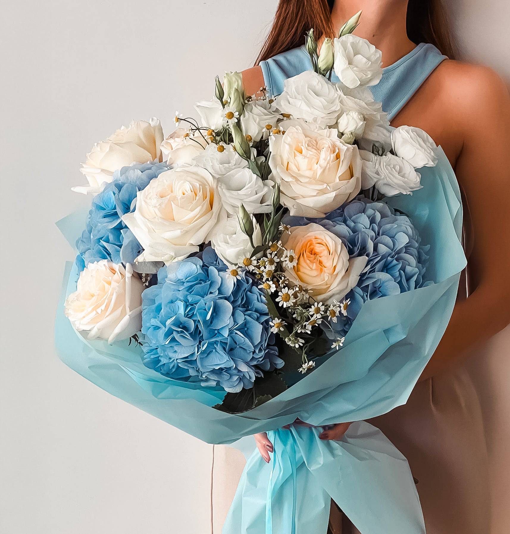 Blue Joy bouquet with blue hydrangeas, white roses, and peach ranunculus wrapped in blue paper