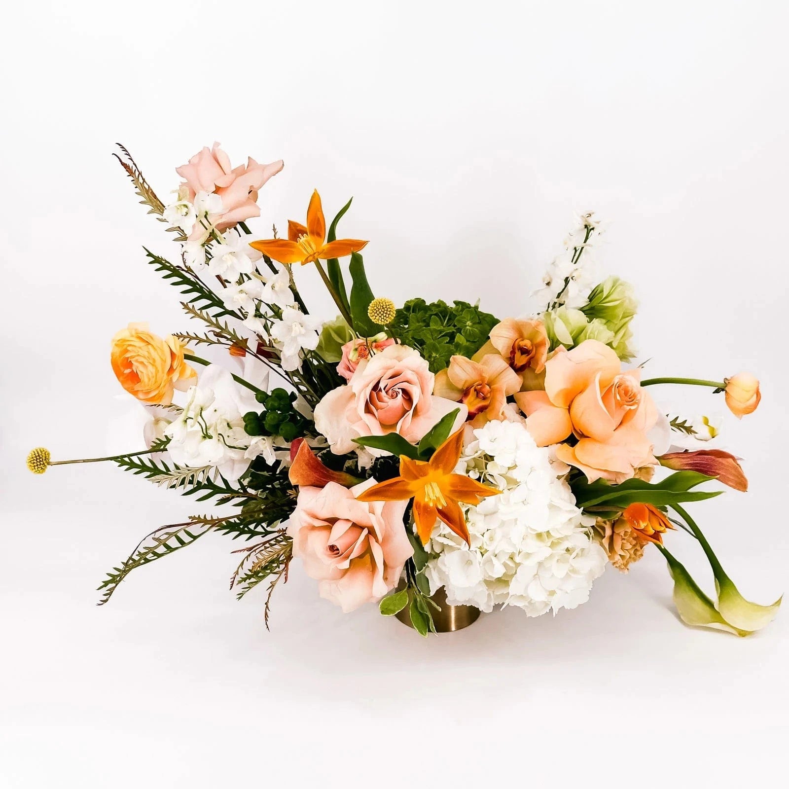 Golden Elegance floral centerpiece featuring peach roses, orange lilies, calla lilies, and white hydrangeas in a modern gold vase.