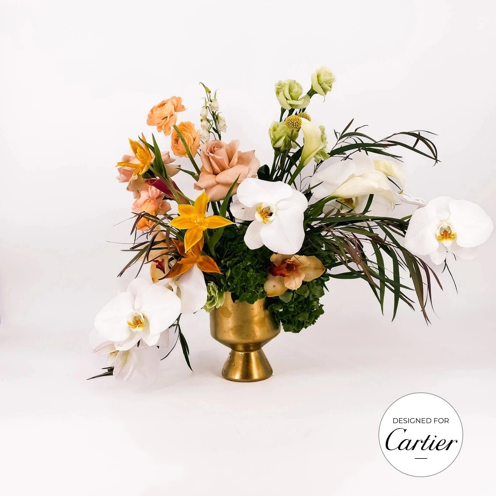 Golden Elegance small arrangement with white orchids, peach roses, orange lilies, and hydrangeas in a gold vase, designed for Cartier by Flowers Valley.