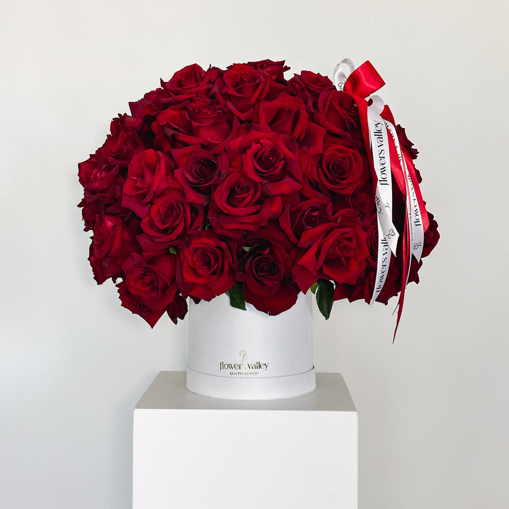 100 red roses arranged in a white hatbox with red and white ribbon from Flowers Valley