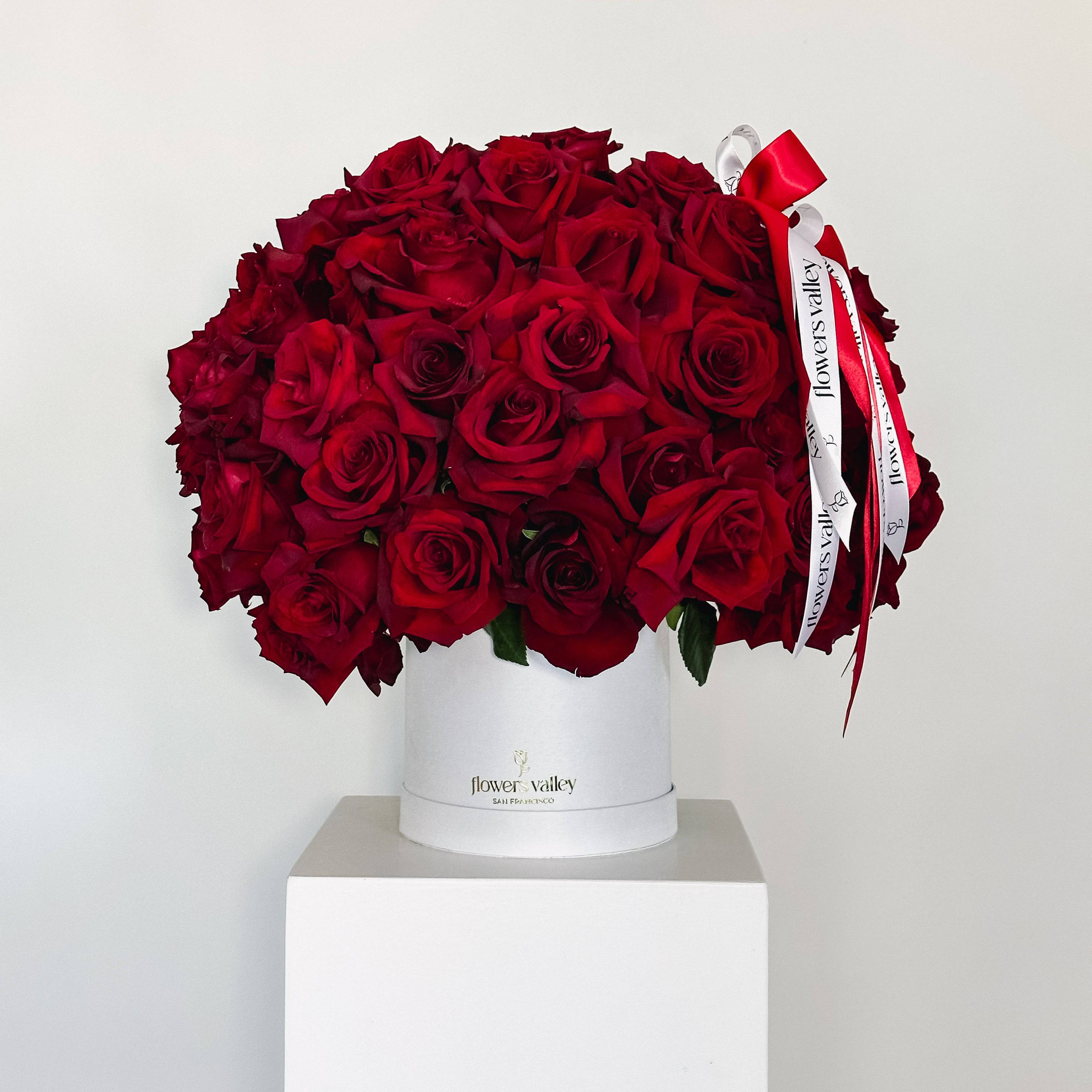 100 red roses arranged in a white hatbox with red and white ribbon from Flowers Valley