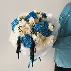 Celeste Bloom bouquet with blue hydrangeas, white lisianthus, and freesias wrapped in white paper