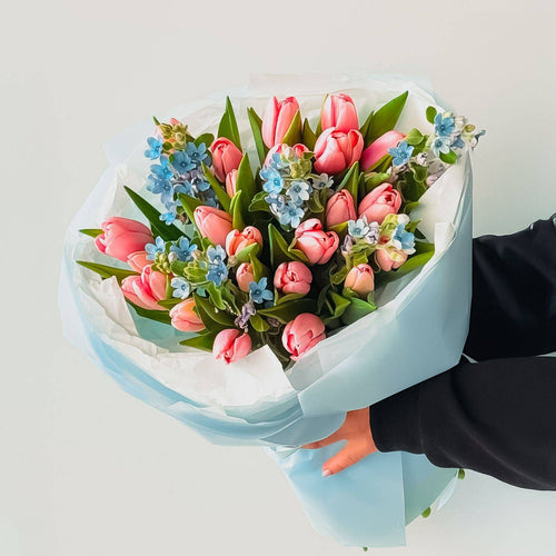 Blush Sky bouquet with pink tulips and blue delphinium wrapped in blue paper