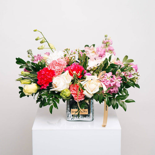 Colorful flower arrangement with pink and white blooms in a white vase, styled on a pedestal