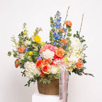 Spring Melody basket with coral ranunculus, mimosa, roses, and delphinium
