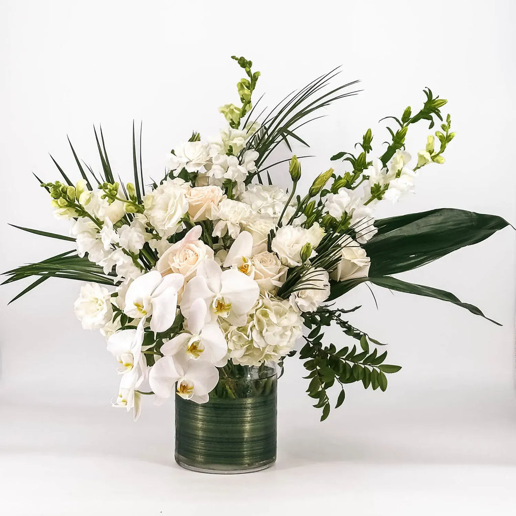 Bouquet of white flowers with greenery in a clear vase on a light background