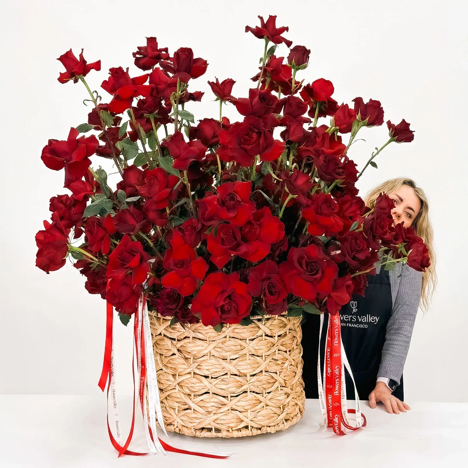 Large bouquet of reflected red roses in a woven basket with a florist behind.