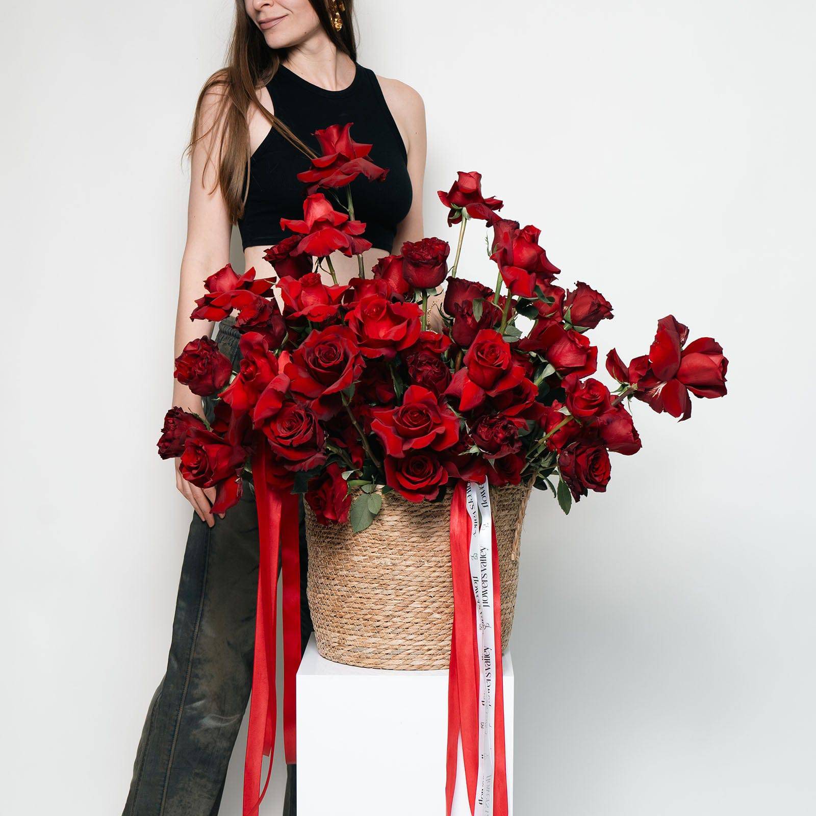 Woman holding a large flower box filled with lush red roses and red ribbon—luxury romantic floral arrangement.