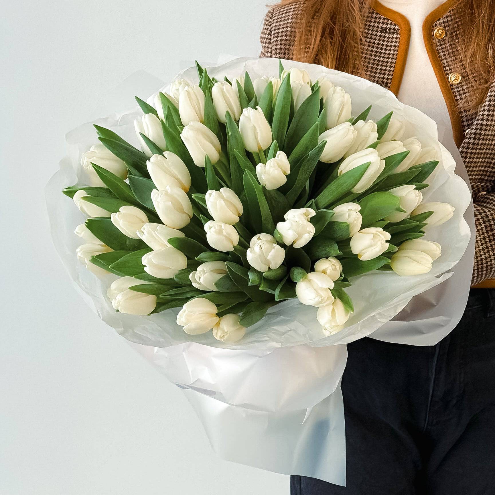 Person holding a bouquet of white tulips wrapped in white paper—simple, elegant, and fresh.