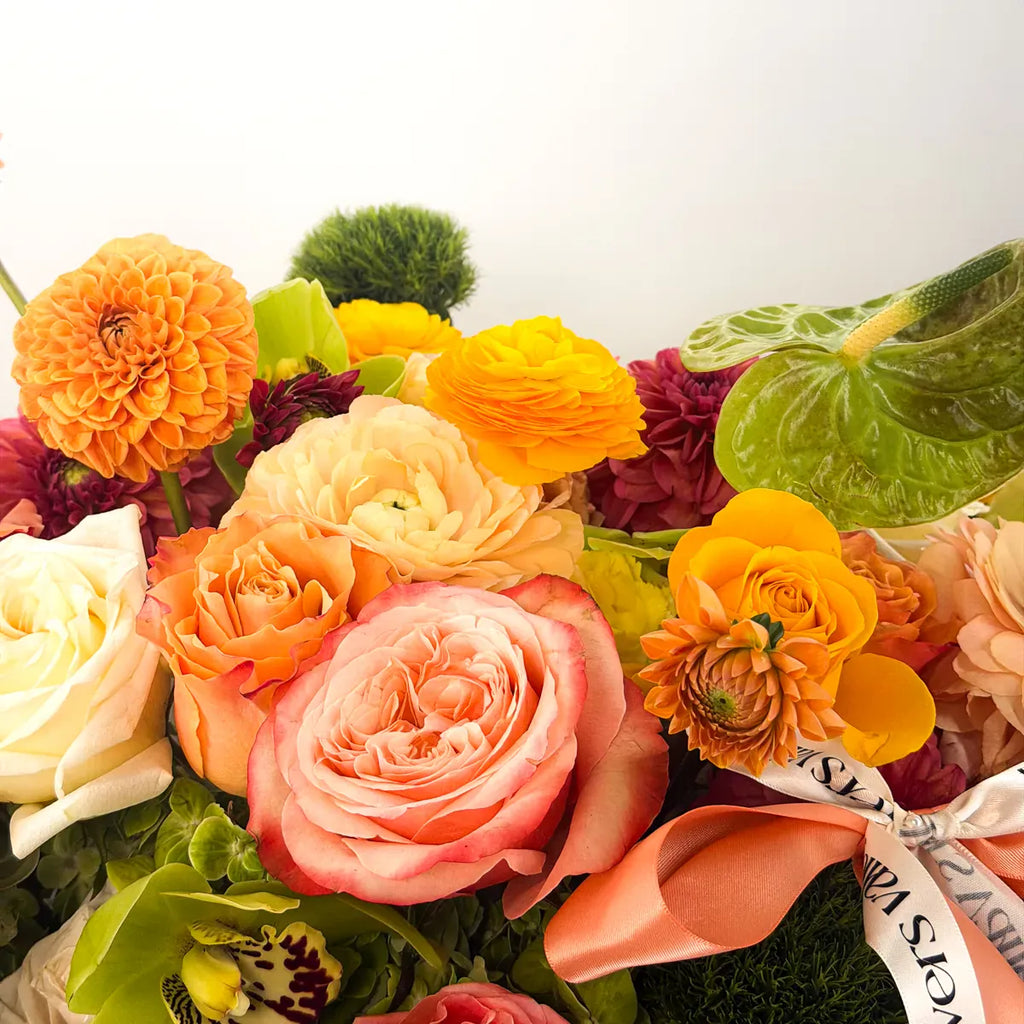 Close-up of a peach garden rose, orange ball dahlia, apricot ranunculus, and green anthurium in the Flowers Valley Apricot Orchard basket