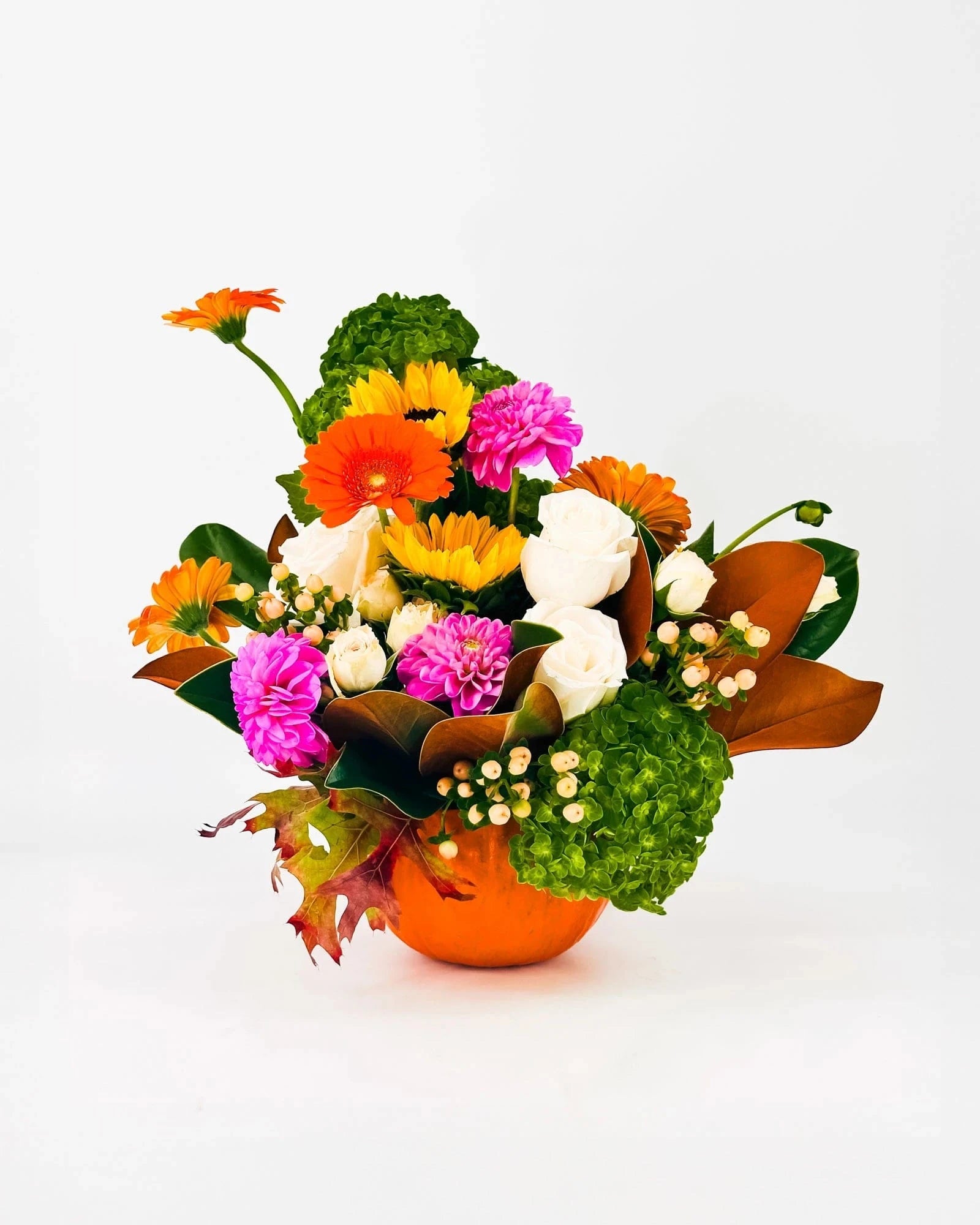 Side angle of Autumn Cheer Pumpkin Arrangement with orange and pink flowers and greenery