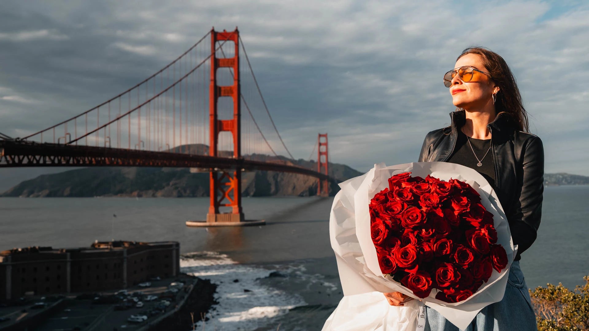 Woman holding a bouquet of red roses with the Golden Gate Bridge in the background