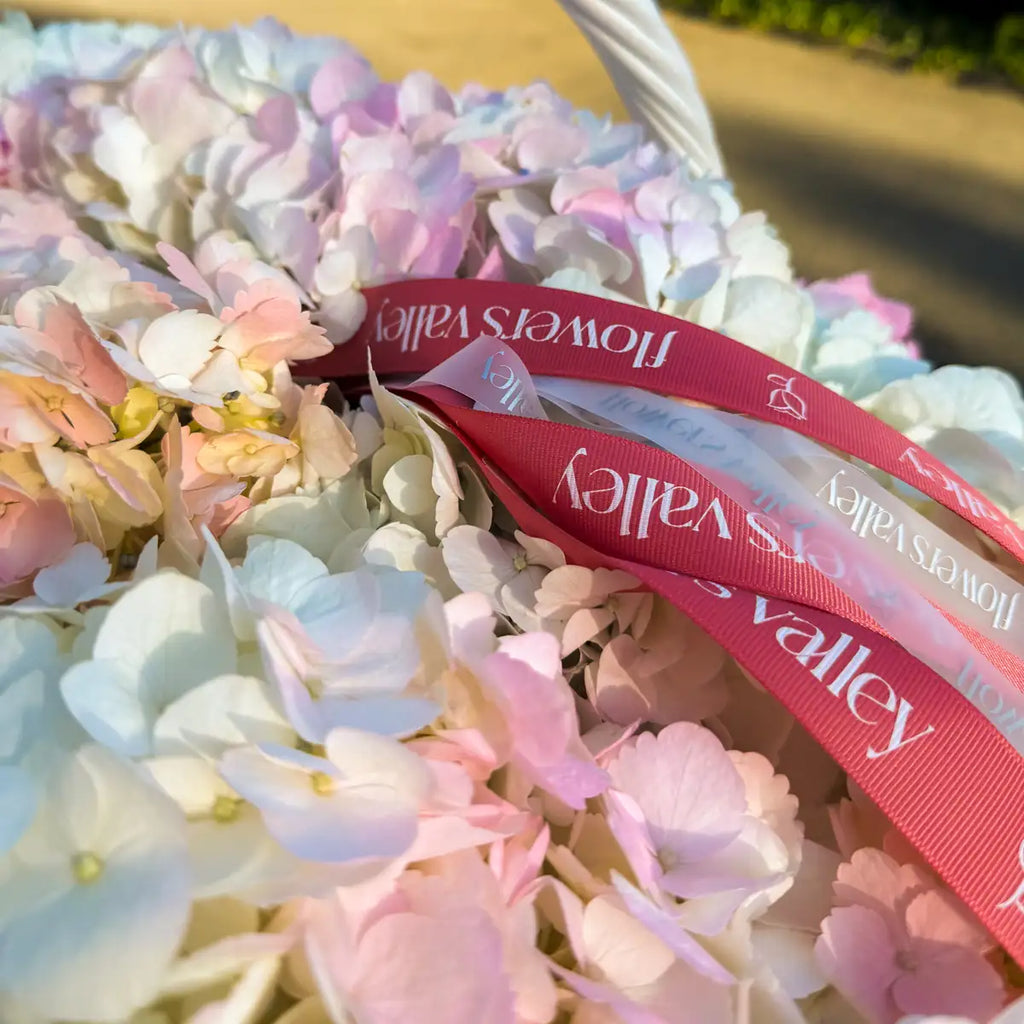 Close-up of blush pink and white hydrangea blooms with the Flowers Valley signature ribbon in a wicker basket