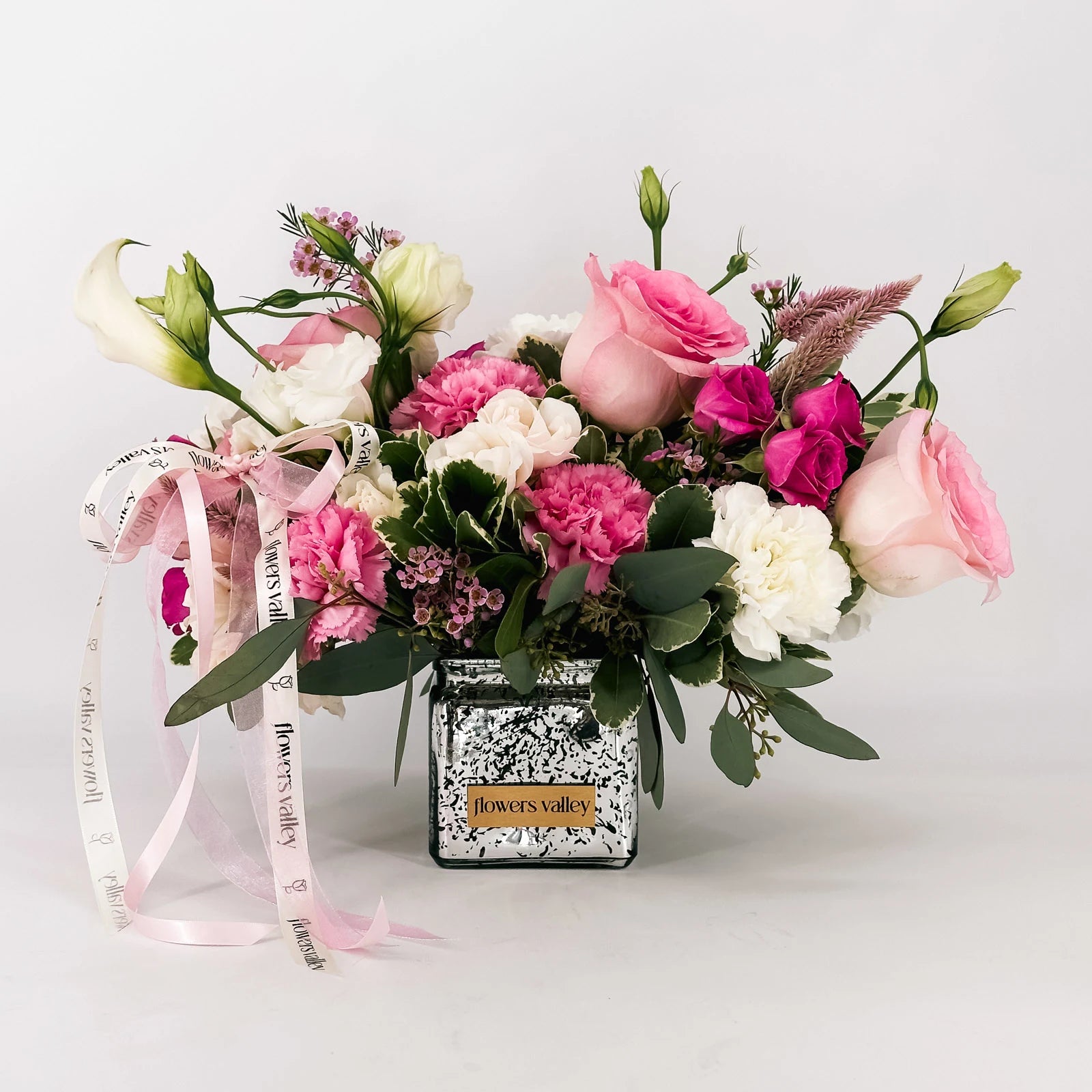 Blushing Grace bouquet featuring blush roses, pink spray roses, carnations, and lisianthus in a mirrored vase with Flowers Valley ribbon.