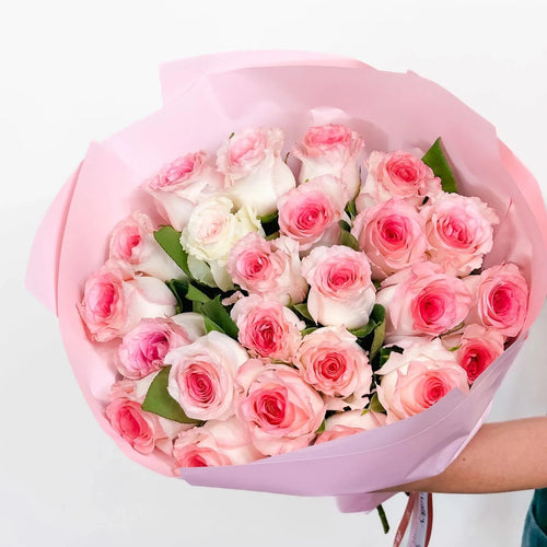 Blushing petals - 24 pink roses in a pink wrap hold by a florist - perfect gift for any occasion, available for same-day delivery 