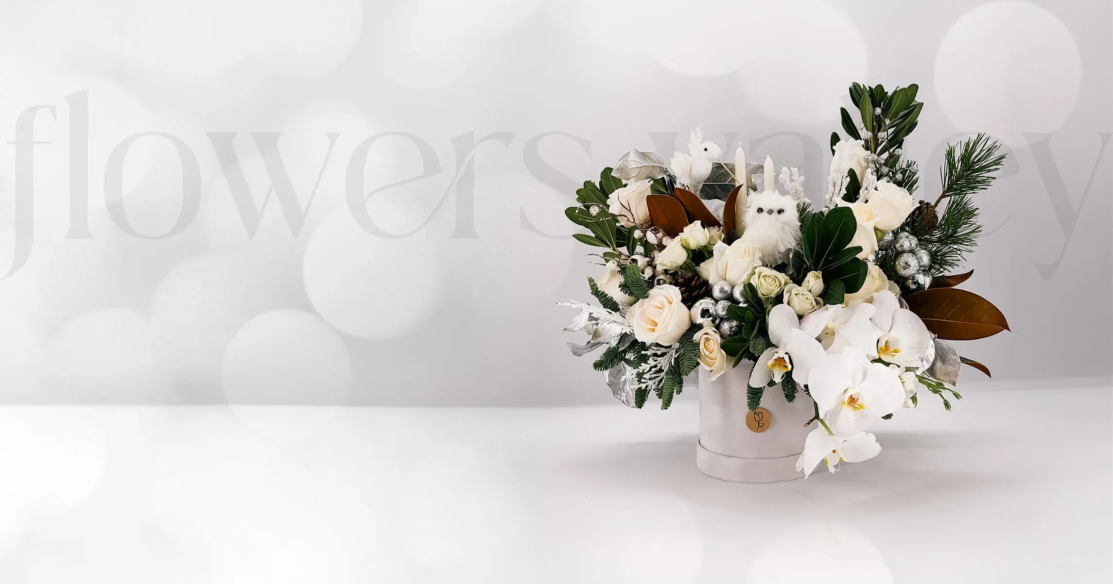 Floral arrangement with white flowers and greenery on a white background, featuring the brand 'flowers by'.