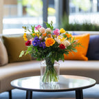Bright coffee table flower arrangement with colorful mixed blooms including roses, tulips, and seasonal greenery in a clear vase – Flowers Valley