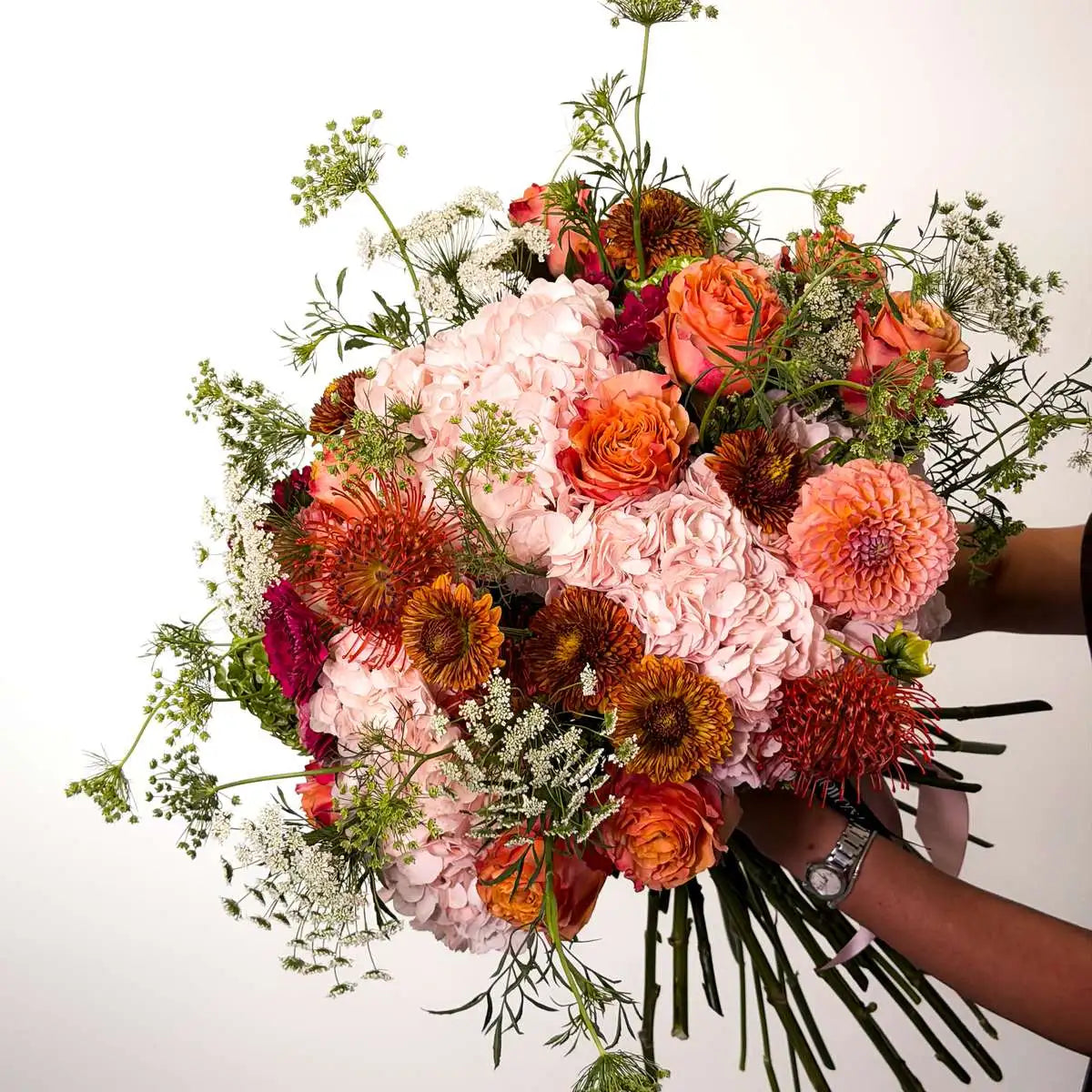 Hand-tied Copper Rosé bouquet held by a florist, showing pink hydrangea, peach dahlia, rust protea and Queen Anne's lace — same-day flower delivery San Francisco Bay Area