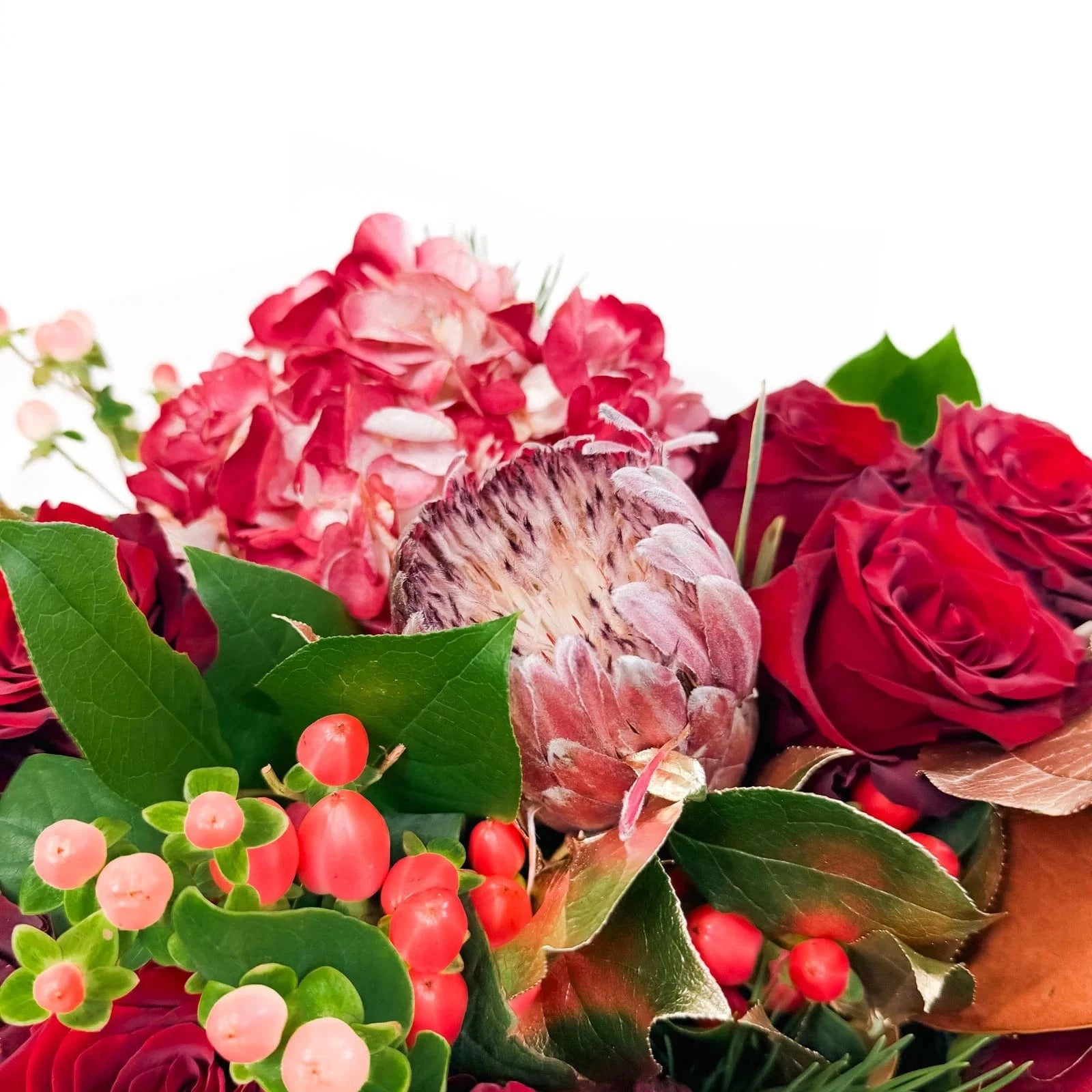 Close-up of Crimson Majesty Bouquet featuring protea, roses, berries, and gold foliage