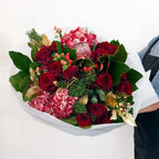 Side angle of Crimson Majesty Bouquet with festive gold leaves and red flowers