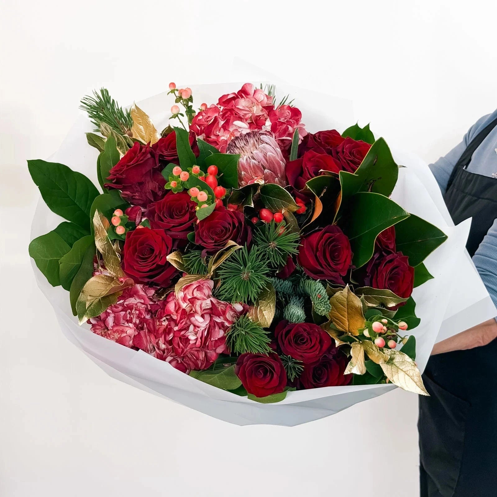 Side angle of Crimson Majesty Bouquet with festive gold leaves and red flowers