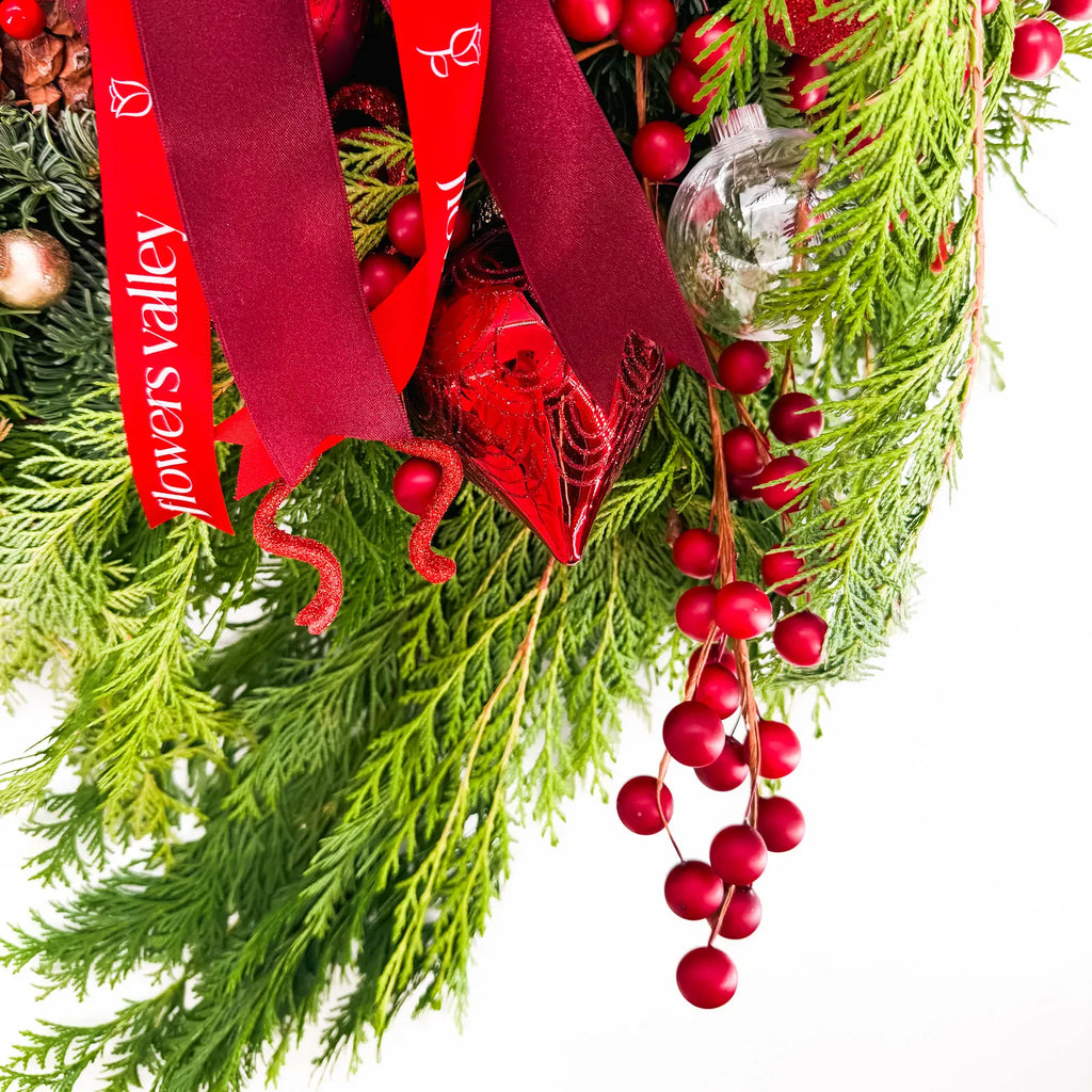 Close-up of Crimson Noel Wreath with winter greenery, berries, and red ribbon accents