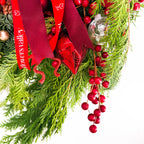 Close-up of Crimson Noel Wreath with winter greenery, berries, and red ribbon accents