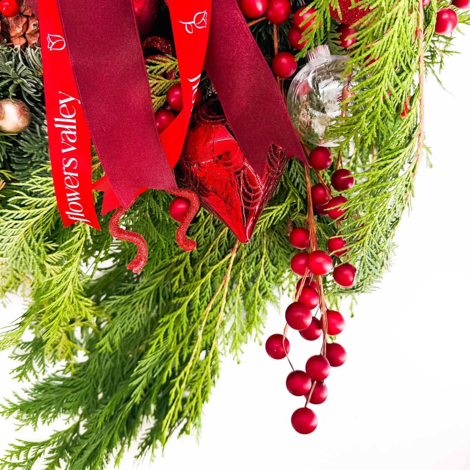 Close-up of Crimson Noel Wreath with winter greenery, berries, and red ribbon accents