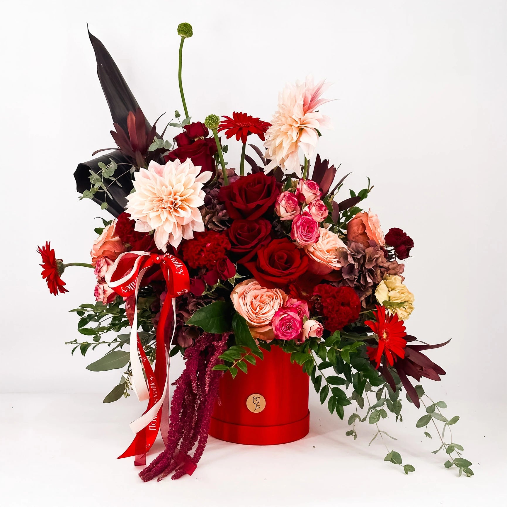 Crimson Symphony luxury flower arrangement with red roses, blush dahlias, spray roses, and gerbera daisies in a red hat box by Flowers Valley.