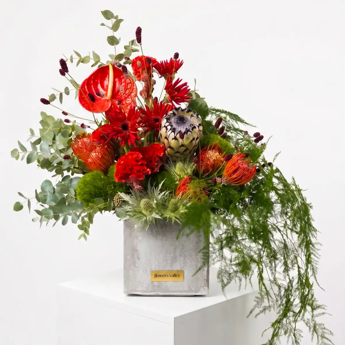 Modern red and orange vase arrangement with anthurium, gerbera, and pincushion protea in a concrete cube by Flowers Valley Bay Area florist