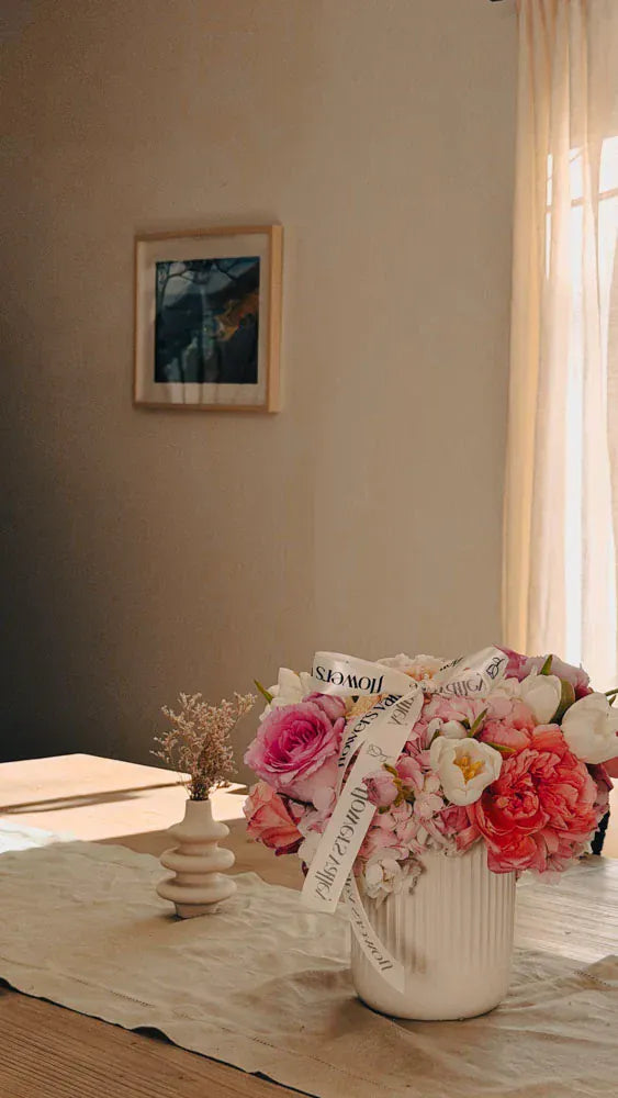 Floral arrangement in a vase on a table with a neutral wall and framed picture in the background.