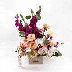 Side view of Majestic Allure premium bouquet with peach roses, magenta stock flowers, and white orchids arranged in a designer vase.