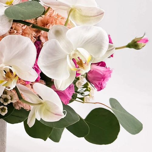 Close-up of Majestic Allure bouquet showing white orchids, pink spray roses, and lush greenery for an elegant floral texture.