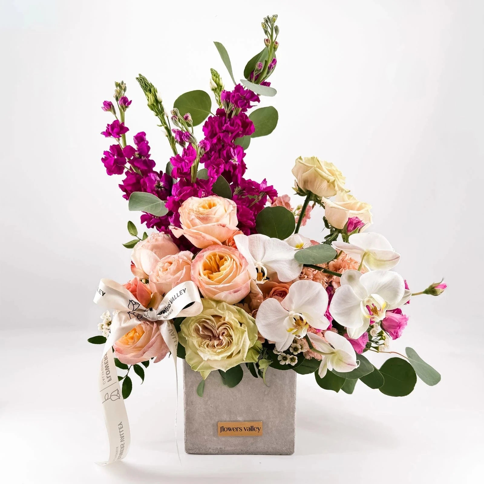 Majestic Allure luxury flower arrangement by Flowers Valley featuring roses, orchids, lisianthus, and peach blooms in a modern concrete vase.