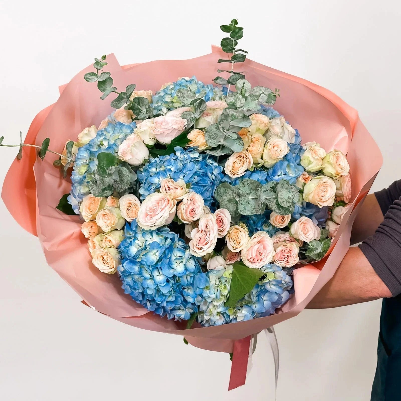 Double the Blooms version of Peach Garden Bouquet with lush peach roses, blue hydrangeas, and premium greenery for a fuller look.