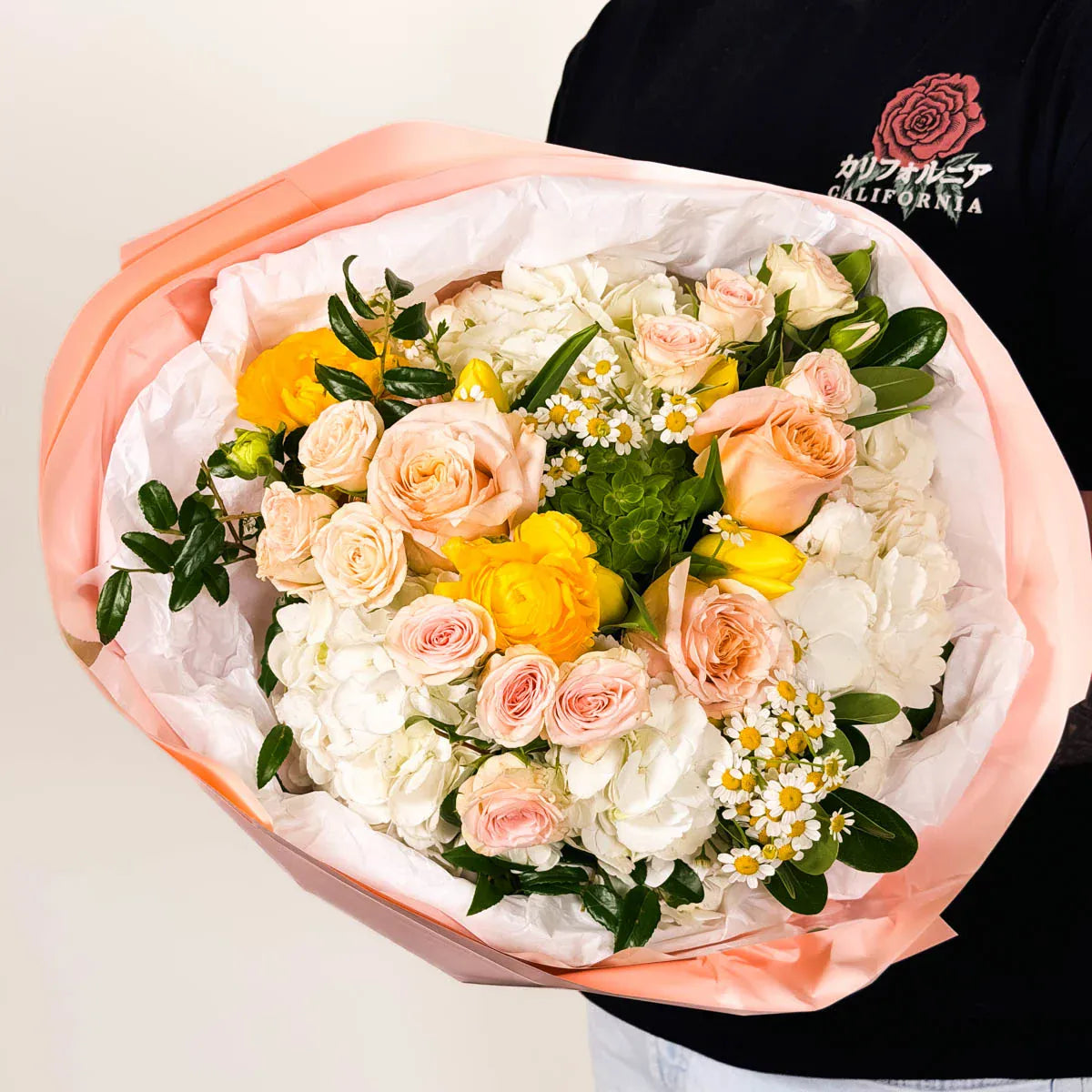 Bouquet of flowers held by a person wearing a black shirt with a brand logo.
