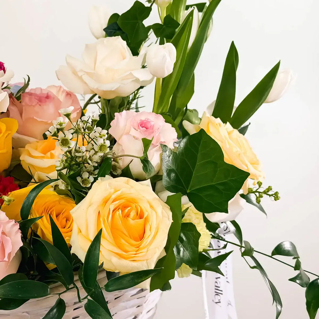 Close-up of yellow roses, pink spray roses, and waxflower detail in the Garden Bloom Flower Basket by Flowers Valley