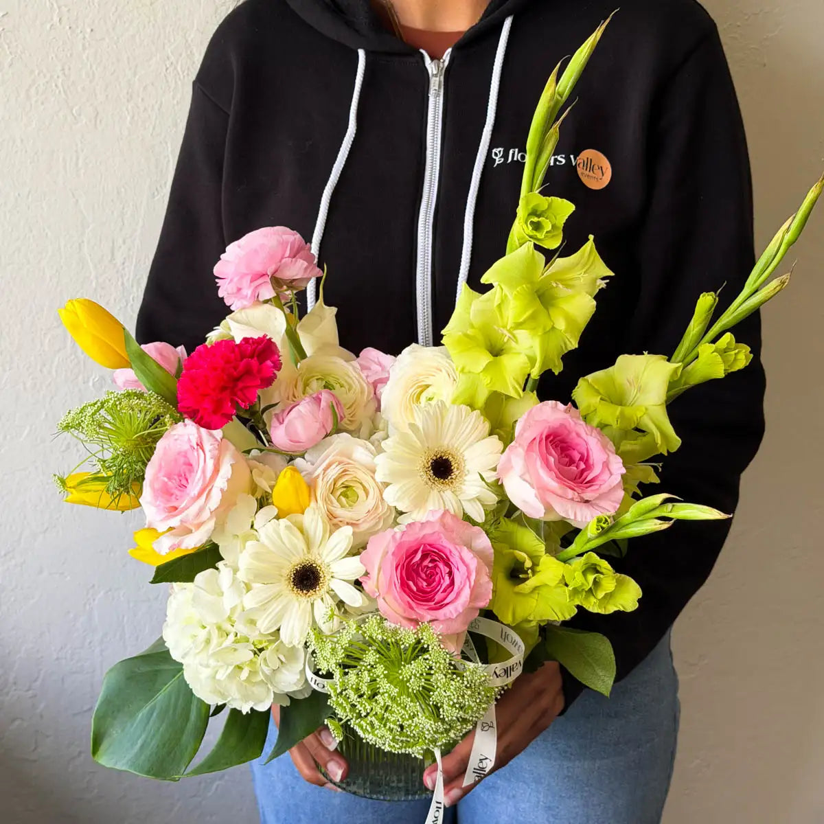 Flowers Valley florist holding the Garden Waltz vase arrangement with pink garden roses, ranunculus, white hydrangea, and green gladiolus stems