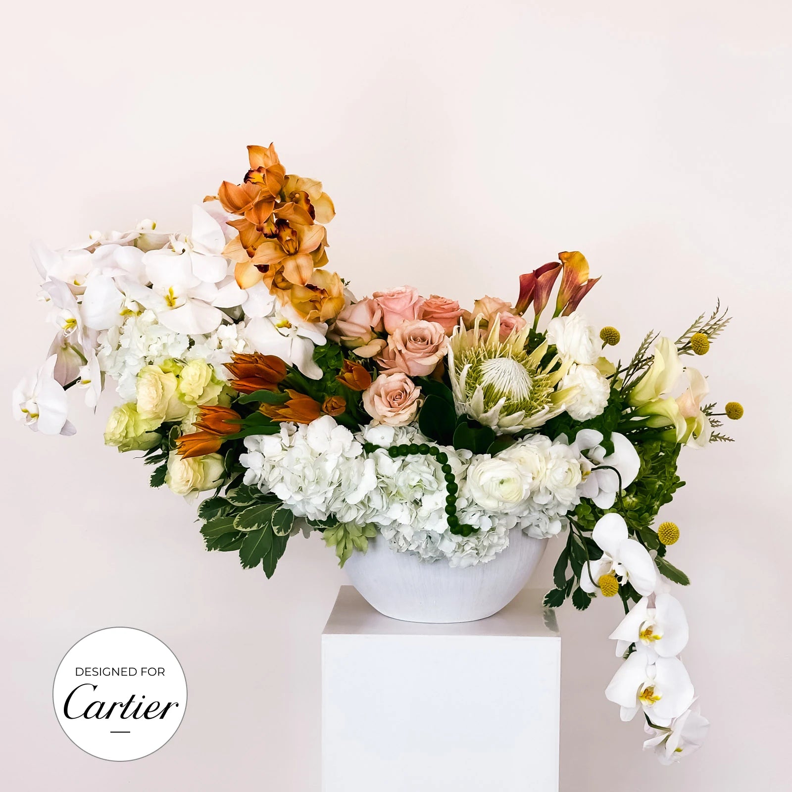 Golden Elegance large floral arrangement with cascading orchids, peach roses, protea, and hydrangeas in a white ceramic vase, designed for Cartier by Flowers Valley.