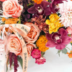 Close-up view of Golden Hour Elegance arrangement with peach roses, cymbidium orchids, dahlias, and spray roses