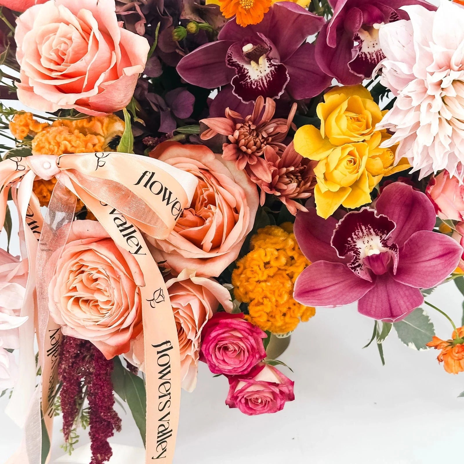 Close-up view of Golden Hour Elegance arrangement with peach roses, cymbidium orchids, dahlias, and spray roses