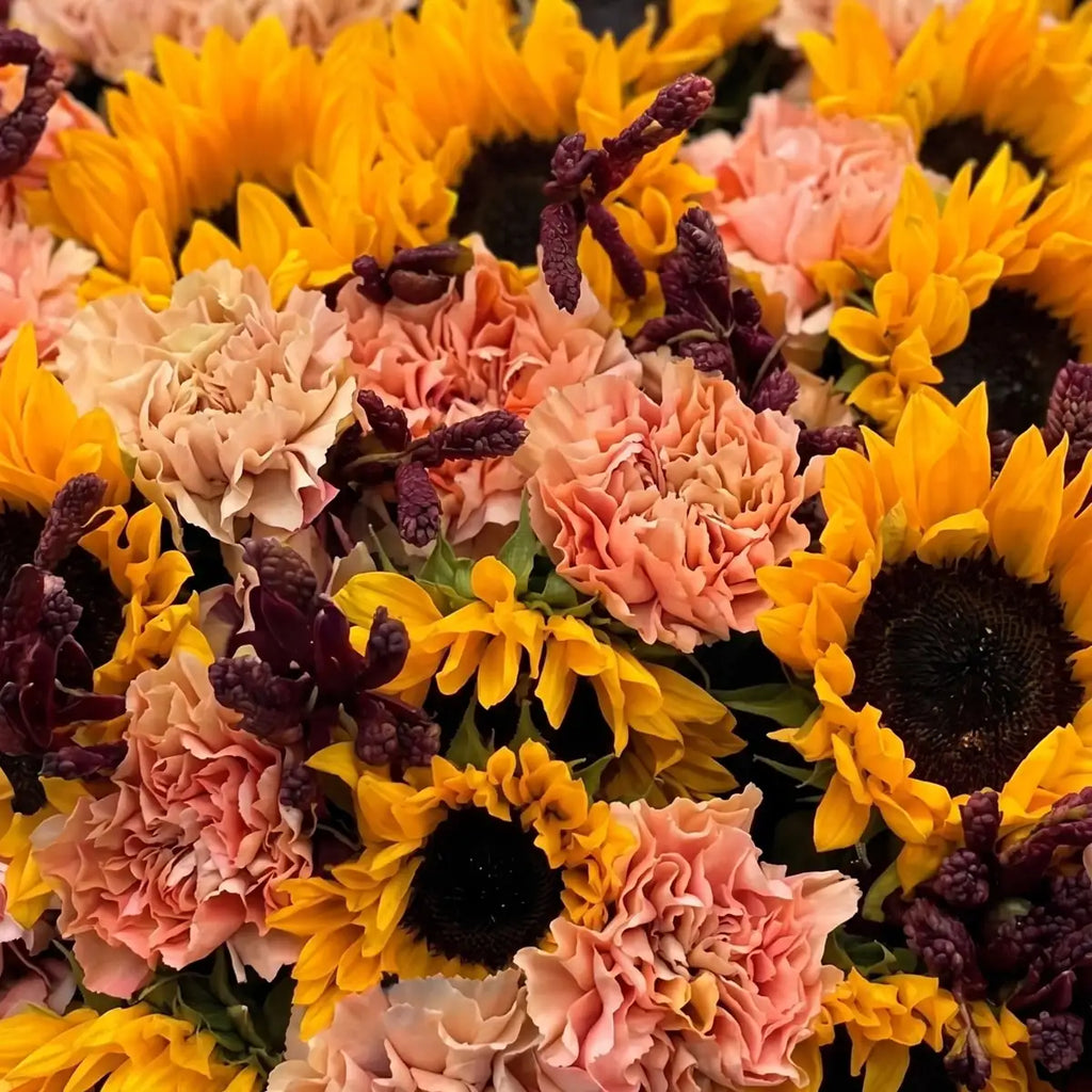 Close-up of golden sunflowers, peach carnations, and burgundy leucadendron in the Golden Hour flower basket by Flowers Valley