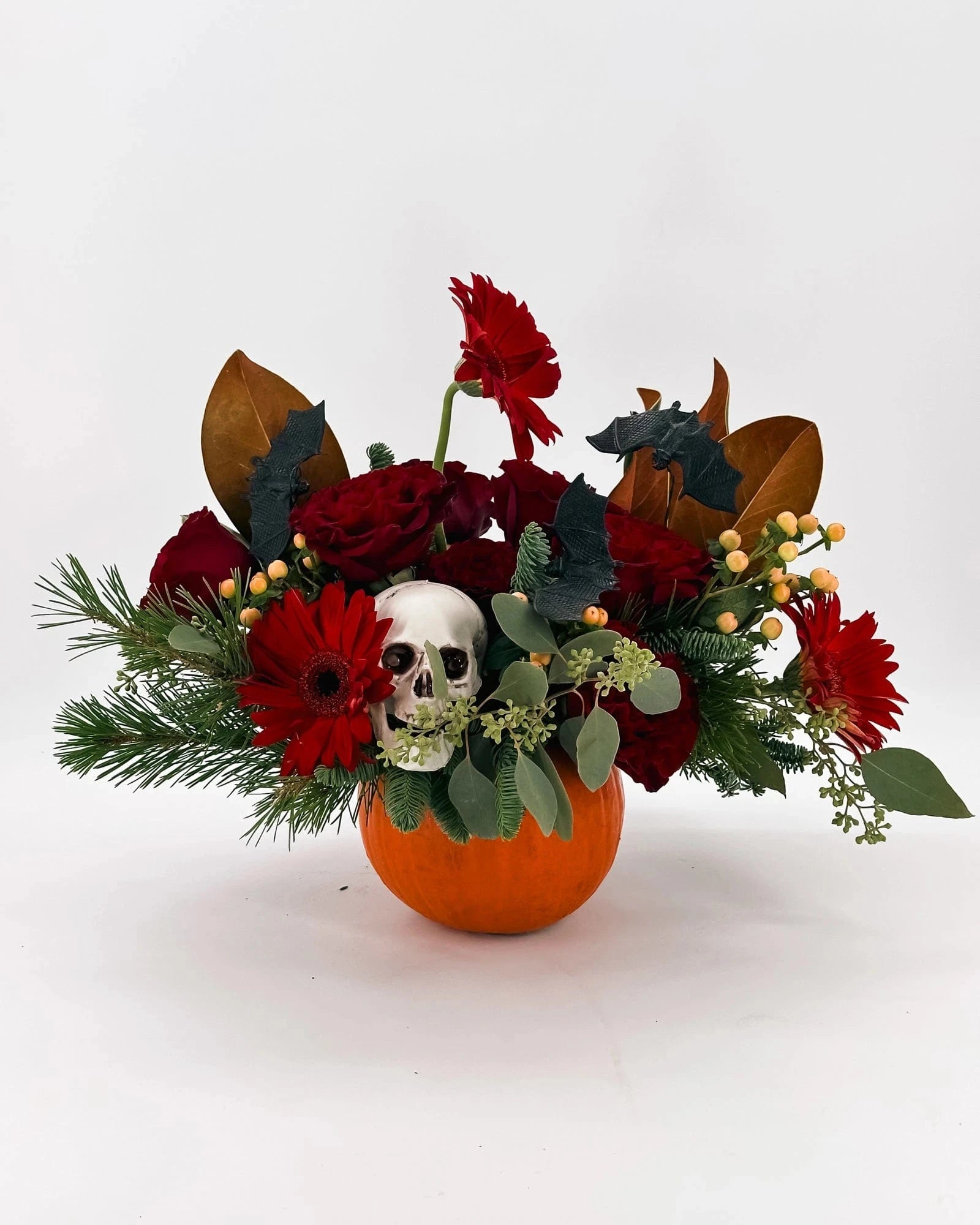 Side angle of Haunted Elegance Pumpkin Arrangement with roses, gerberas, skull, and greenery