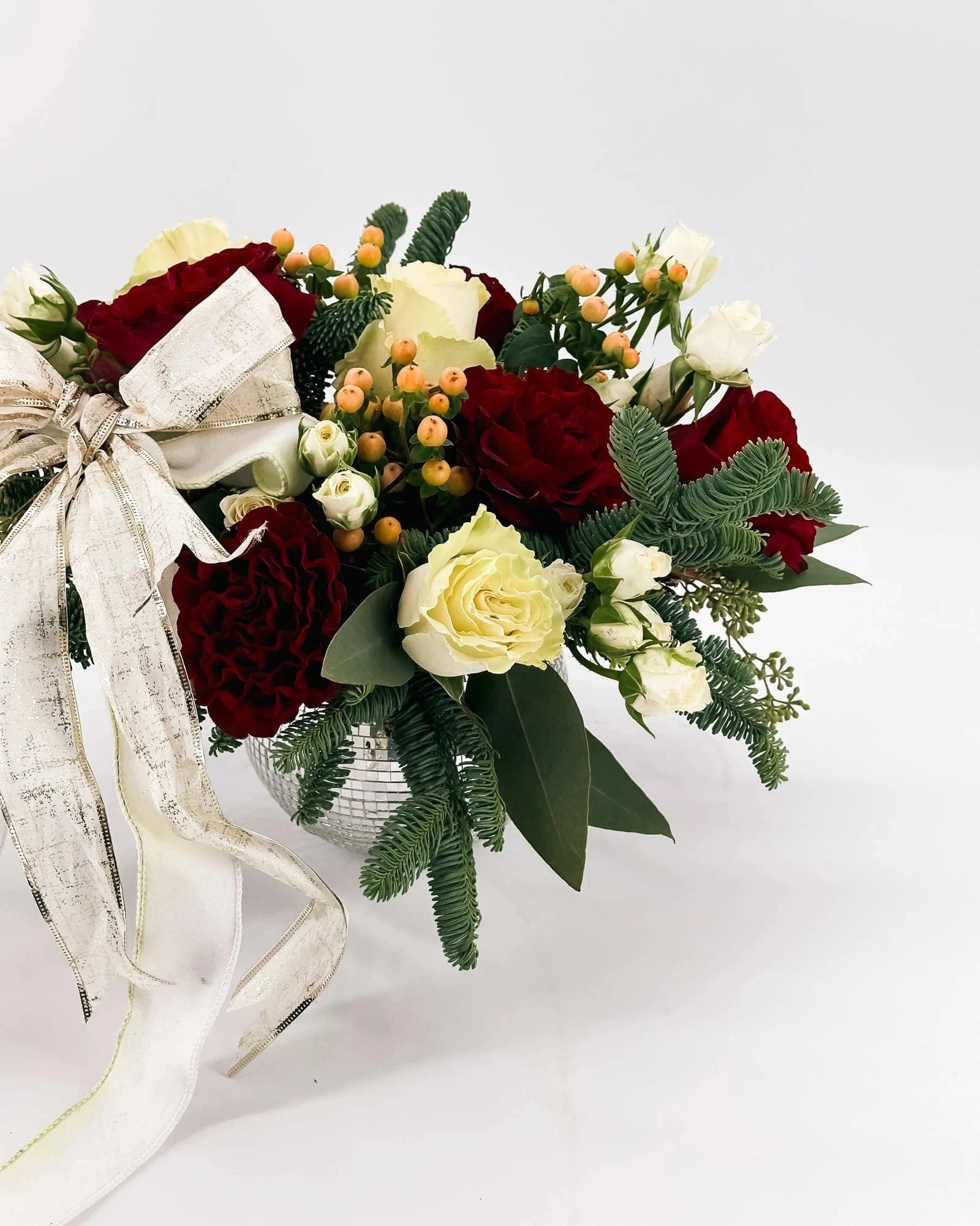 Side view of Holiday Enchantment Arrangement with roses, berries, evergreens, and gold bow