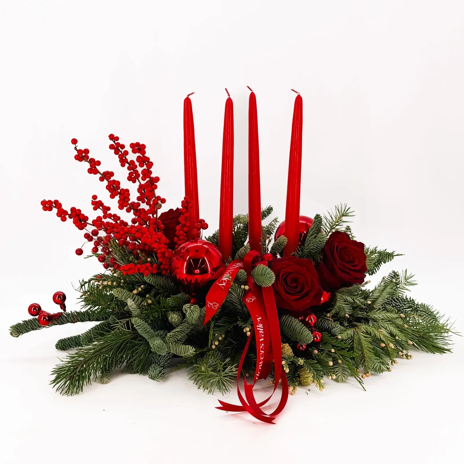 Luxury holiday centerpiece with red roses, winter evergreens, ornaments, and four red taper candles