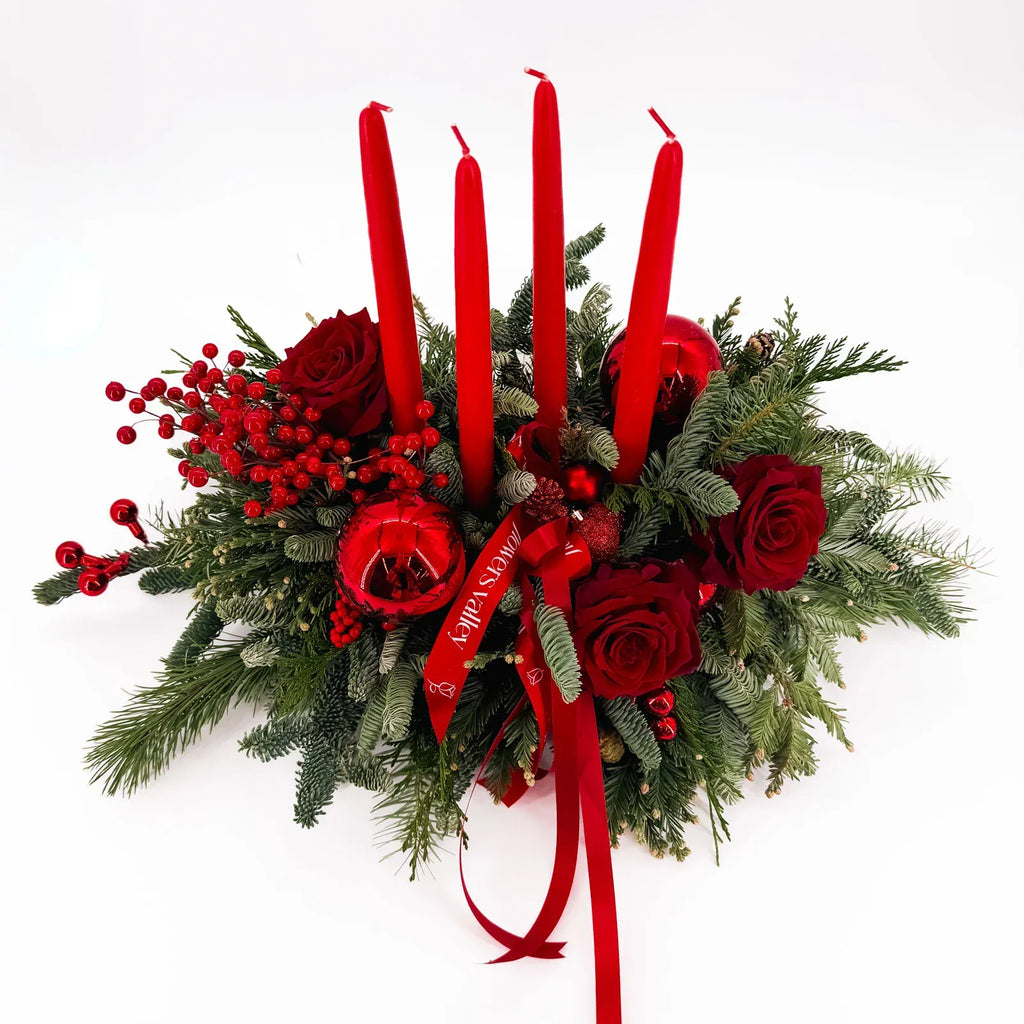 Christmas table arrangement with red candles, red berries, and lush winter greenery