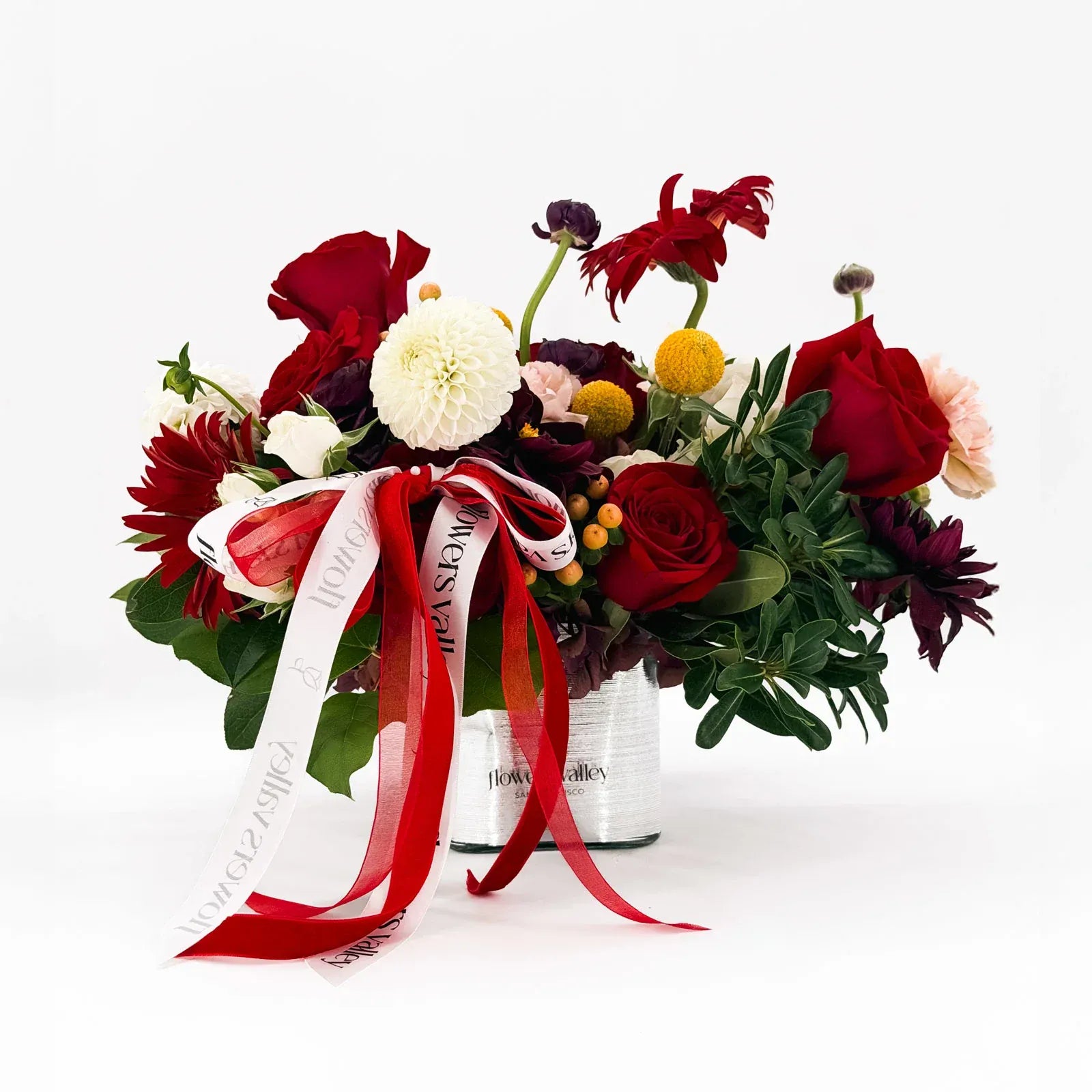 Holiday Muse Arrangement with red roses, dahlias, and festive ribbons in glass vase