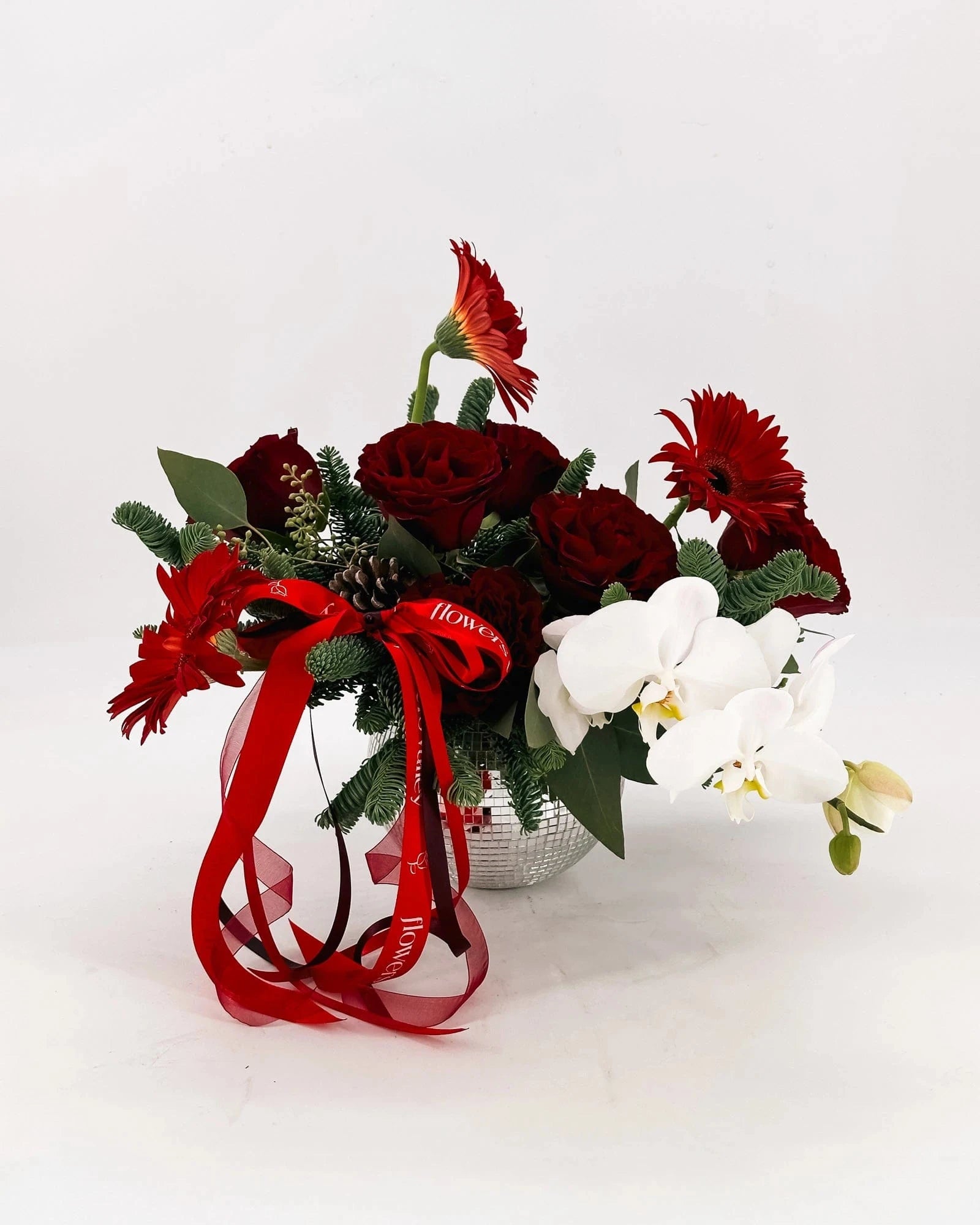 Holiday Radiance Arrangement with red roses, gerbera daisies, orchids, and holiday accents