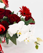 Close-up of white phalaenopsis orchids with red roses and evergreens in Holiday Radiance Arrangement