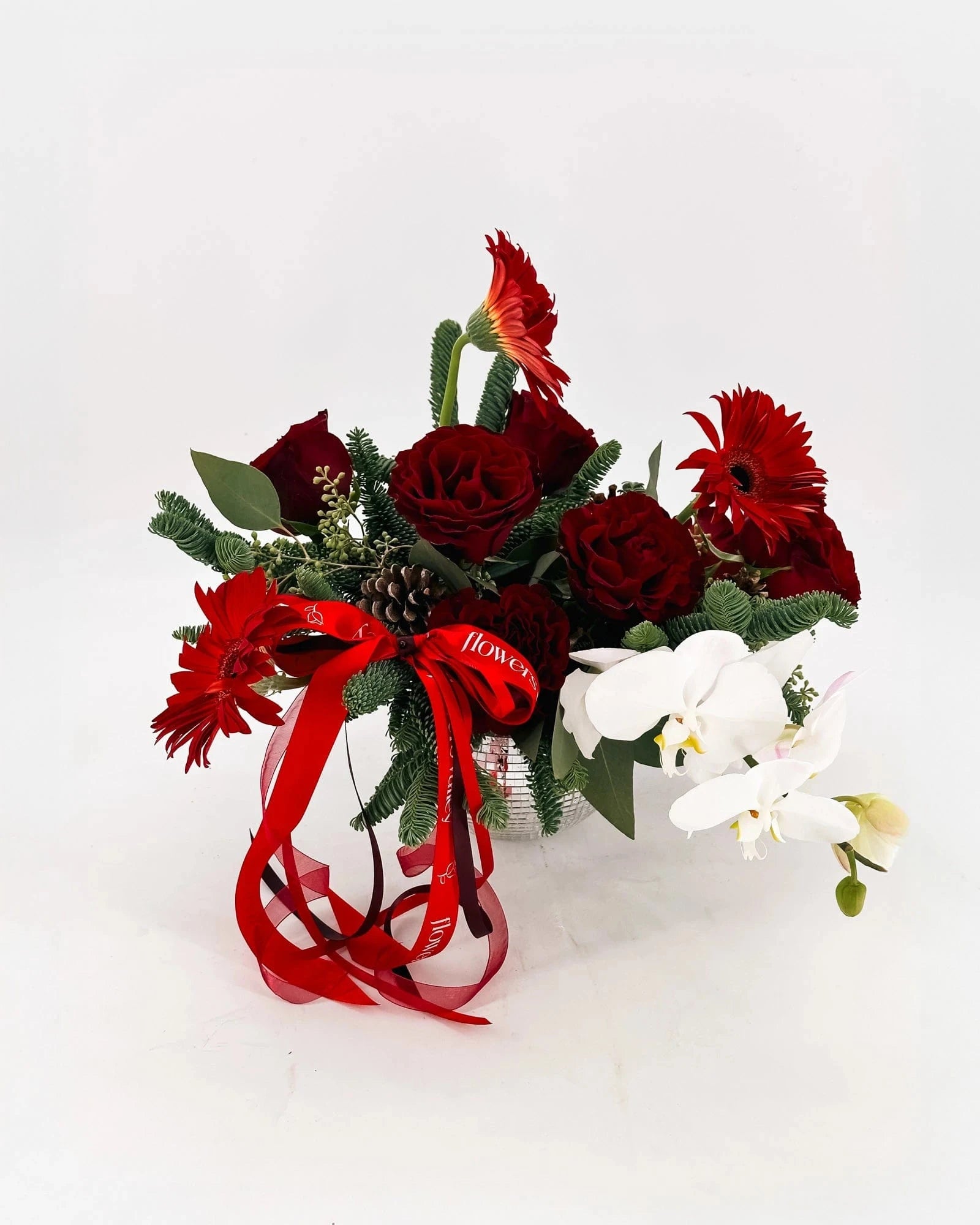 Side view of Holiday Radiance Arrangement in a silver vase with orchids and red blooms